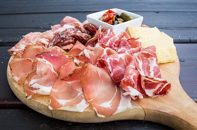 A wooden board of cured hams, salami and cheese
