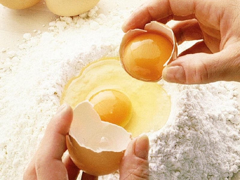 An egg cracked into a well of flour, the first step of fresh pasta
