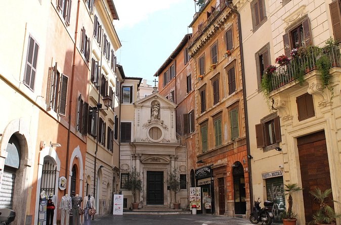 A narrow Roman street of ochre houses ending at a small church front