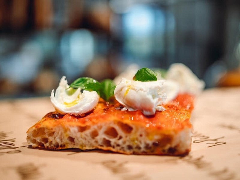 A slice of Roman pizza topped with burrata and a basil leaf