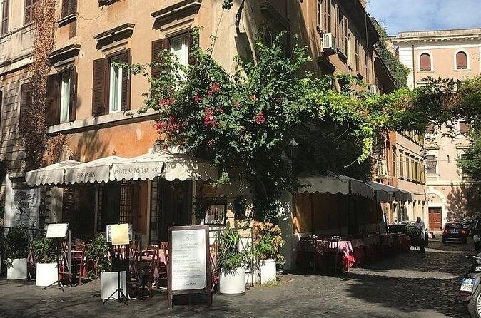 Trattoria awnings and tables under a bougainvillea on a quiet Roman street