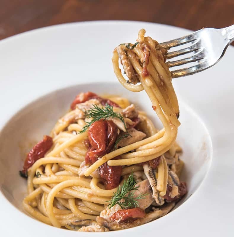 Spaghetti with tomato twirled on a fork above the bowl